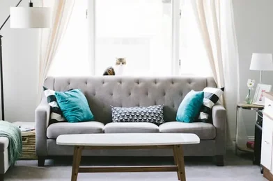 Sofa nỉ xám ba chỗ với gối tựa xanh ngọc và bàn trà gỗ trong phòng khách