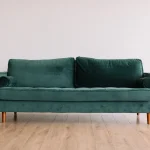 Sofa nỉ màu xanh rêu ba chỗ ngồi kê sát tường trắng trên sàn gỗ sáng